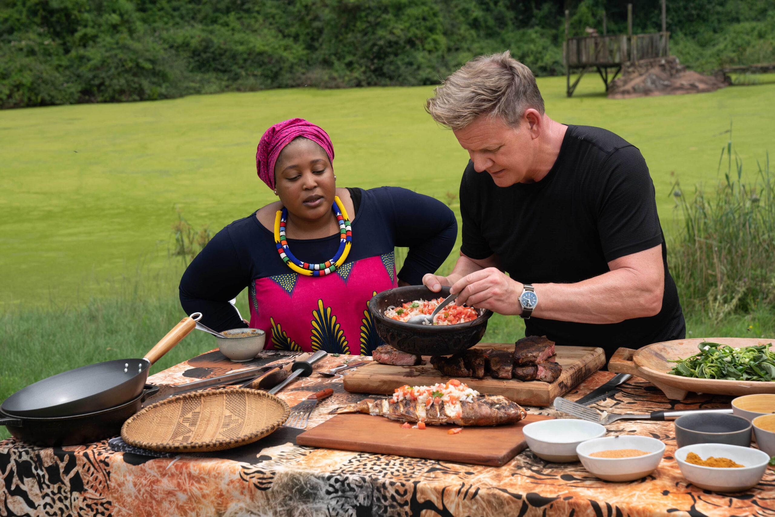 Gordon Ramsay in Sud Africa per 'Gordon Ramsay: Fuori Menù' - chef Zola Nene (sinistra) osserva come Gordon Ramsay guarnisce il pesce alla griglia con ushatini, una combinazione di cipolle e pomodori [credit: National Geographic/Jon Kroll; courtesy of Disney Italia]